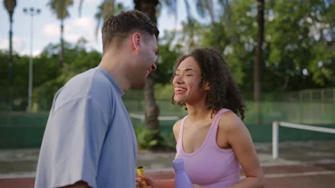 Smiling athletic couple laughing together on tennis court during summer break 動画素材 325157151