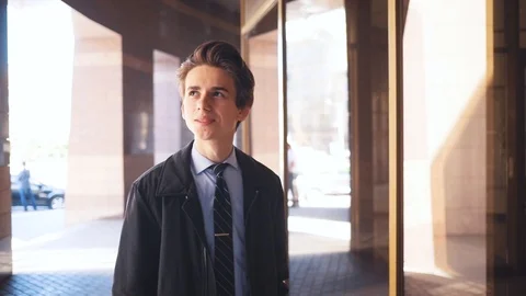 Smiling attractive. Caucasian guy walking near building, looking at smart watch Stock Footage 92059922