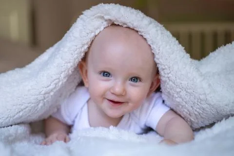Smiling baby looking at camera under a white blanket, towel Stock Photos