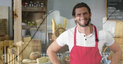 Smiling baker in red apron white-henley behind bakery counter showing loaves Stock Photos