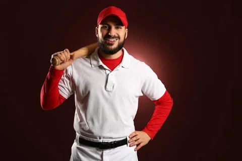 Smiling baseball player in red cap and white uniform holding bat over shoulde Stock Photos