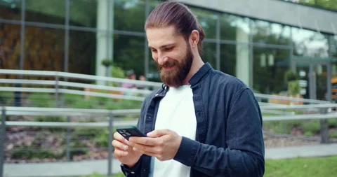 Smiling bearded Caucasian man walking outdoors along an urban street near a mode Stock Footage 327551267