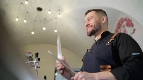 Smiling bearded chef cook dressed black uniform with apron sharpening knife with Video stock 255863691