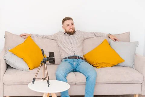 Smiling bearded guy filming video using smartphone on tripod online while Stock Photos