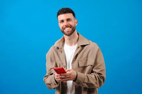 Smiling bearded man holding red smartphone against blue background Stock Photos