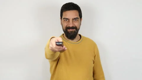 Smiling bearded man holds a remote control in his hand pointing it at the camera Stock Footage 165903273
