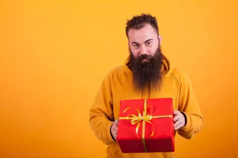 Smiling bearded man looking at the camera and holding a red gift box over yellow Stock-Fotos