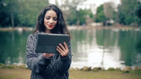 Smiling beautiful brunette using digital tablet at the park Stock Footage 85673963