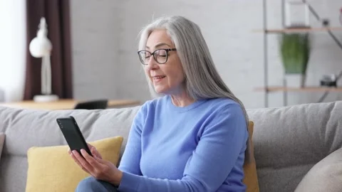 Smiling beautiful elderly gray-haired woman using smartphone for texting message Video stock 164532831