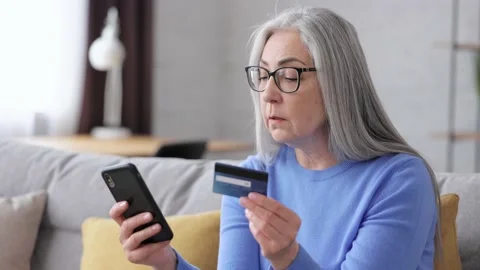 Smiling beautiful elderly gray-haired woman shopping online holding credit card Stock Footage 164532900