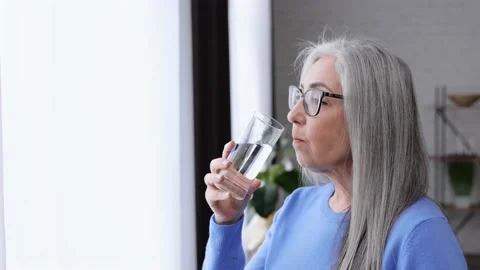 Smiling beautiful elderly gray-haired woman holding glass of water and drinking Video stock 164532994
