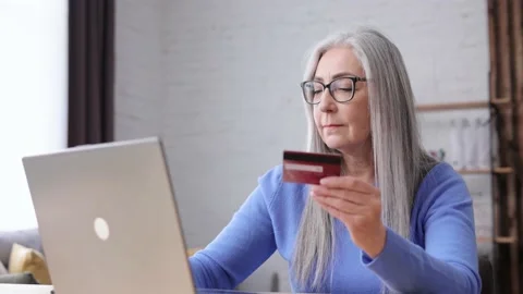 Smiling beautiful elderly gray-haired woman shopping online holding credit card Video stock 164532995
