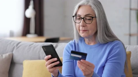 Smiling beautiful elderly gray-haired woman shopping online holding credit card Stock Footage 181508161