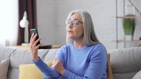 Smiling beautiful elderly gray-haired woman using smartphone for video call 스톡 동영상 213279730