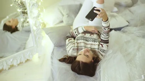 Smiling beautiful lady lying on a decorated floor and taking selfies Stock Footage 69923637