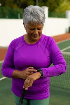 Smiling biracial senior woman with short hair holding tennis racket and checking Stock Photos