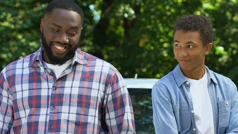 Smiling black dad throwing car keys to teenage son, both getting in vehicle Stock Footage 116206374