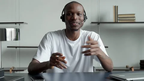 Smiling black man in a headset, working on a laptop and looking at the camera 스톡 동영상 168741699