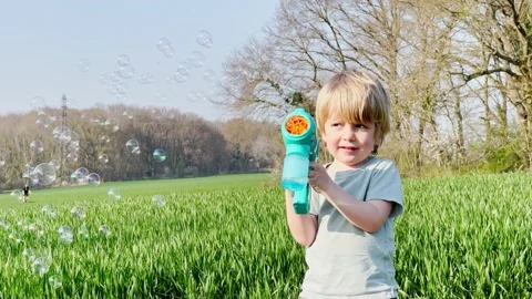 Smiling blond boy play soap bubbles gun on the lawn Stock Footage 204874824