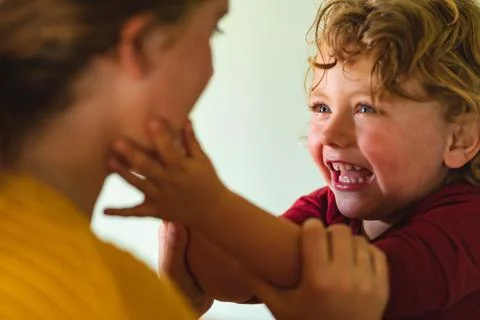 Smiling blond boy playing while touching mother's cheek in kitchen at home Fotos Stock