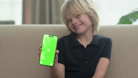 Smiling blonde boy showing iPhone 14 with chroma key green screen and sitting Stock-Footage 231315504