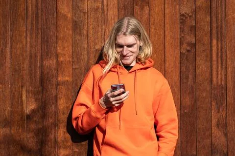 Smiling blonde man use smartphone outside, looks at phone screen, checking Stock Photos