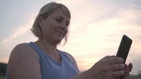 Smiling blonde with short cut hair holding the cellphone in her hands and 스톡 동영상 157442602