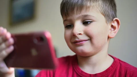 Smiling blonde small boy is watching video in smartphone Stock Footage 250363987