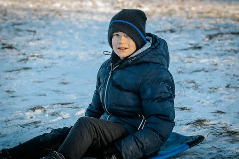 A smiling boy in a black winter jacket and hat sleds downhill on a snow Stock Photos