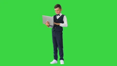 Smiling boy in a bow tie and waistcoat using laptop computer while standing on a Stock-Footage 138542641