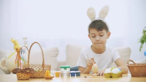 Smiling boy is colorizing an Easter egg with a help of paint-brush., wearing Stock Footage 104637654