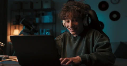 A smiling boy with curly hair wearing wireless headphones works on a school Stockbeeldmateriaal 200863653