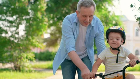 Smiling boy cyclist plays with dad in city park. Child wears helmet, father Vidéo 334343052