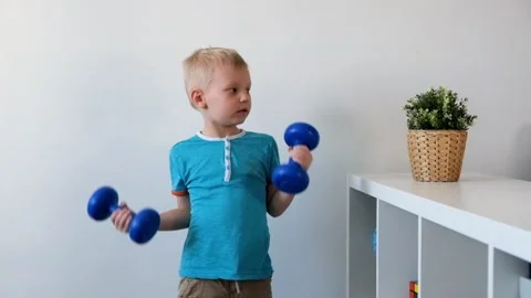 Smiling boy is doing exercises with dumbbells in his room Vídeos de archivo 88392626