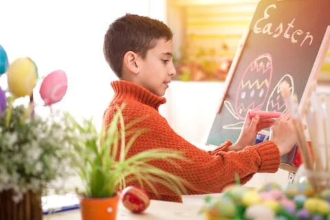 Smiling boy draws easter eggs with chalk on  green chalkboard Stock Photos