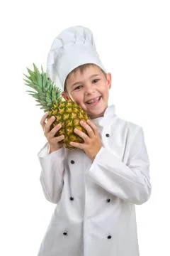 Smiling boy dressed in chef uniform huggs pineapple on white background. Stock Photos