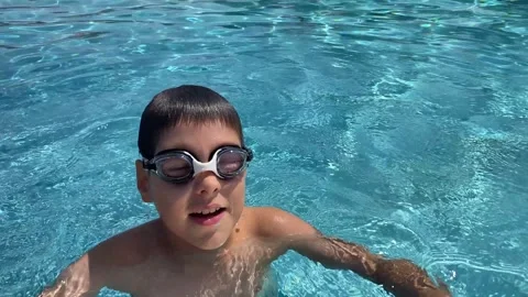 Smiling boy in goggles holds nose to dive in swimming pool and talks to camera Stock Footage 341400852
