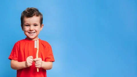A smiling boy with healthy teeth holds a toothbrush on a blue isolated backgr Stock Photos