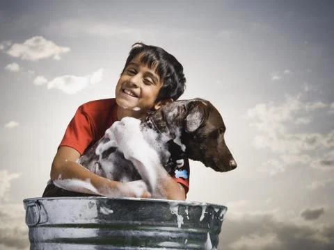 Smiling boy hugging and bathing dog outdoors on cloudy day Stock Photos