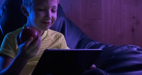 Smiling  boy  looks to the screen tablet  and  eating apple.   Cute child wit Stock Footage 118520961
