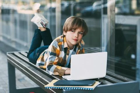 A smiling boy is lying on a bench and preparing for school lessons, next to a Stock Photos
