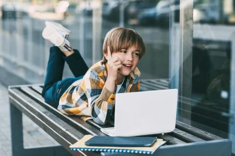 A smiling boy is lying on a bench and preparing for school lessons, next to a Stock Photos
