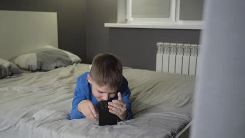 Smiling boy playing online games on a smartphone while lying at home in bed. Stock Footage 261061012