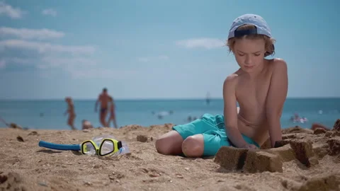 Smiling boy playing with sand on beach, taking diving mask, go to dive in sea Stock Footage 138397096