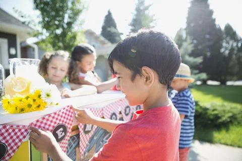 Smiling boy preparing lemonade stand sign in sunny driveway Stock Photos