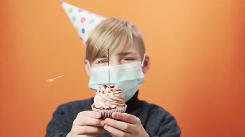 Smiling boy in protective mask holds a cupcake with a burning sparkler. Stock Footage 164380253
