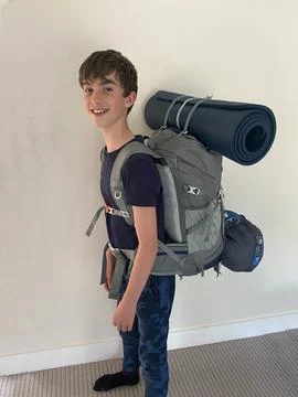 Smiling boy ready for hiking with backpack, sleeping pad and sleeping bag on his Stock Photos