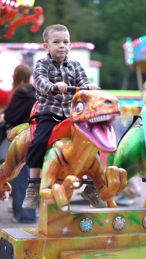  smiling boy riding dinosaur attraction at colorful amusement park Stock Footage 344206462