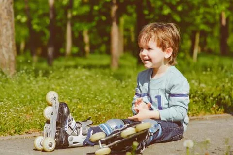 Smiling boy in rollers sits on walkway at park Stock Photos