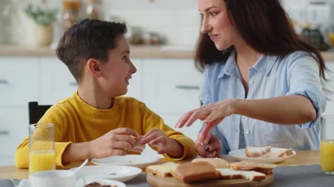 A smiling boy sits at the kitchen table with his mother and eats a sandwich. A Stock Footage 240059266